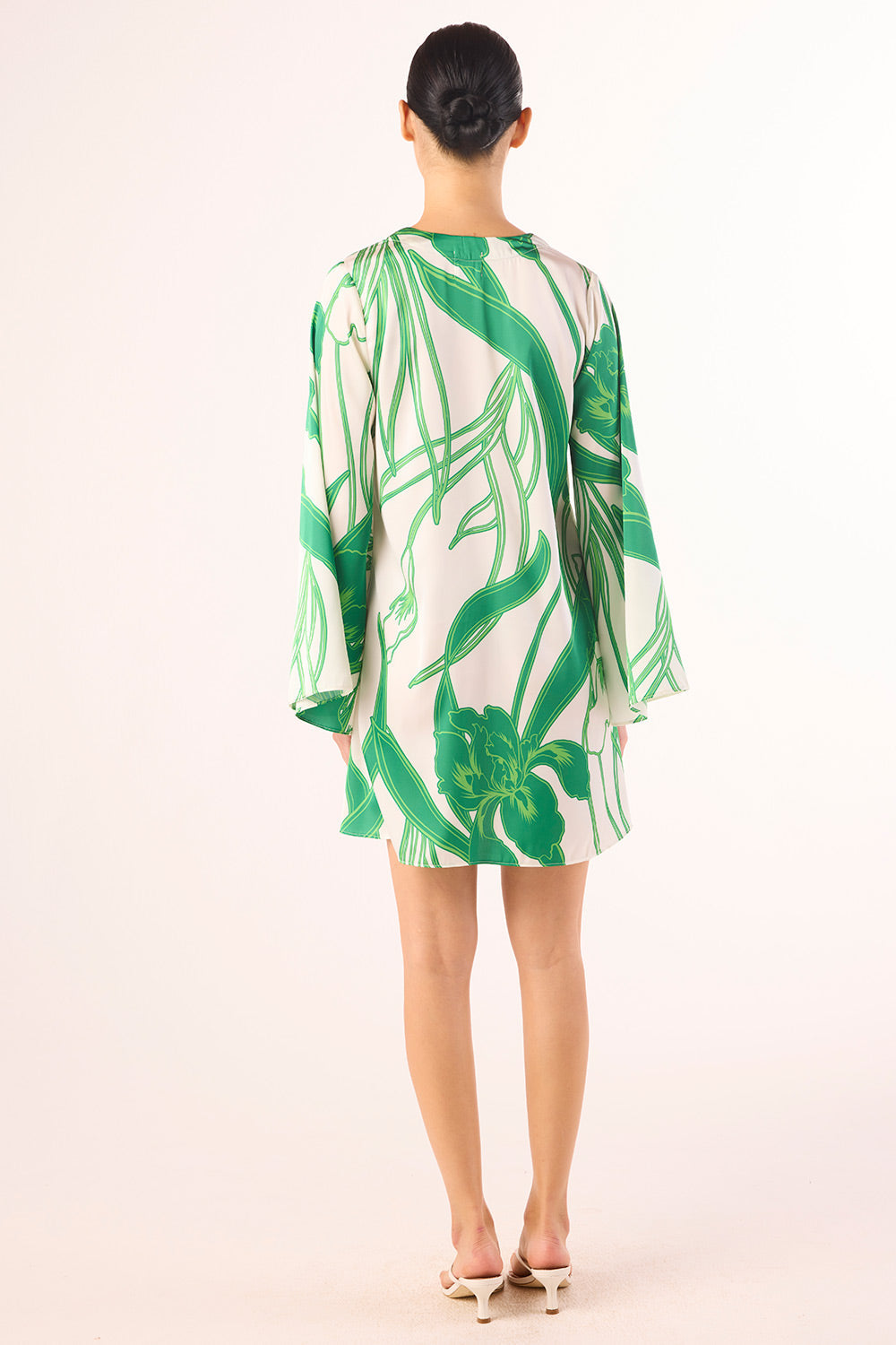 Woman wearing a green and white leaf-patterned dress on a light pink background